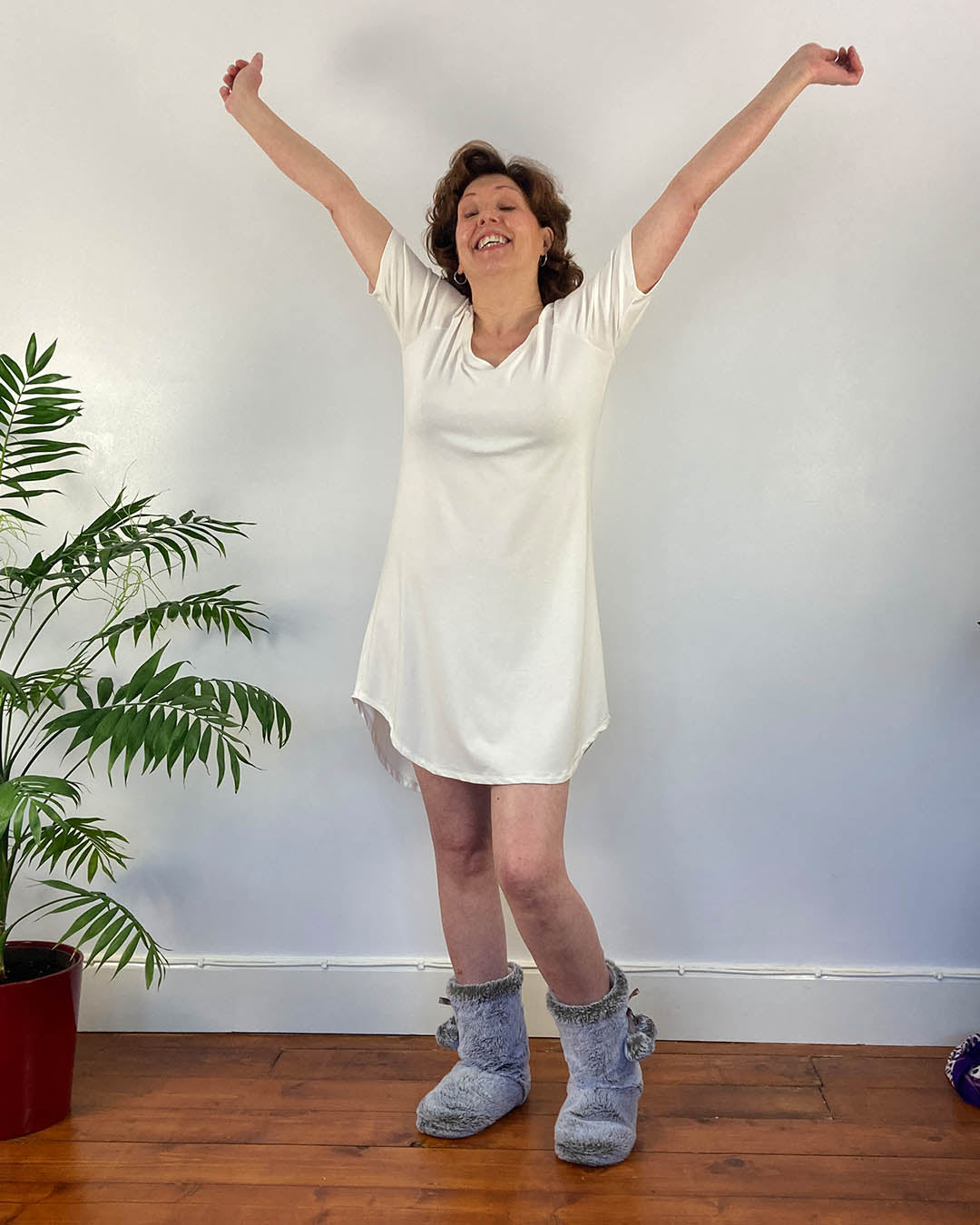 A woman in short white nightie with arms in the air - sleepwear designed to help with menopausal flushing, perimenopause hot flashes and menopause and sweating.